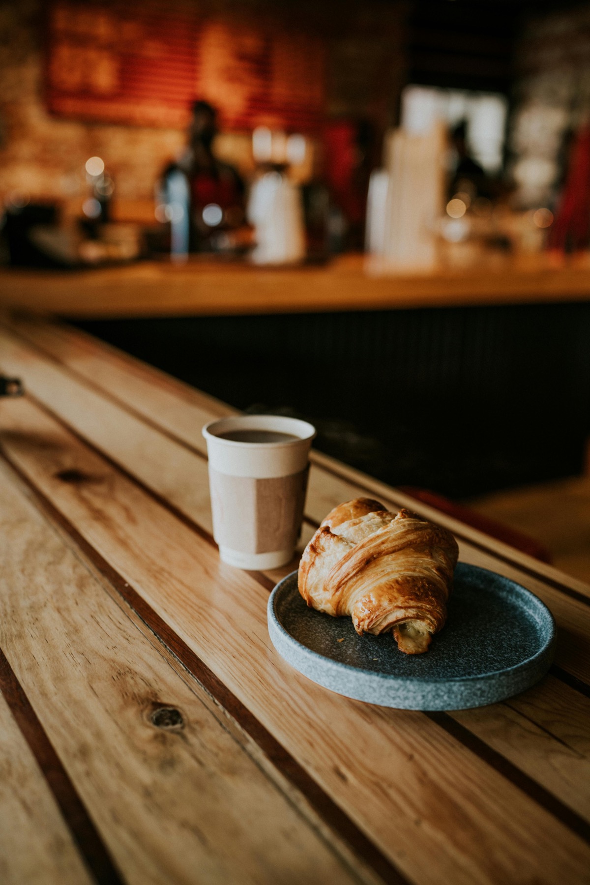 A croissant and a cup of coffee on a wooden table in a cozy cafe